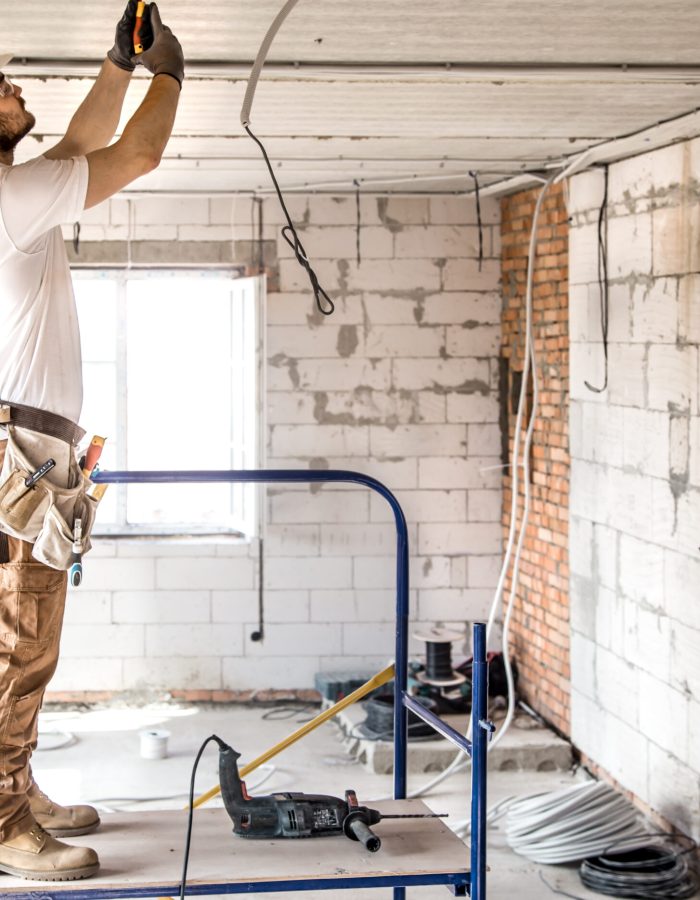 Electrician installer with a tool in his hands, working with cable on the construction site. Repair and handyman concept. House and house reconstruction.