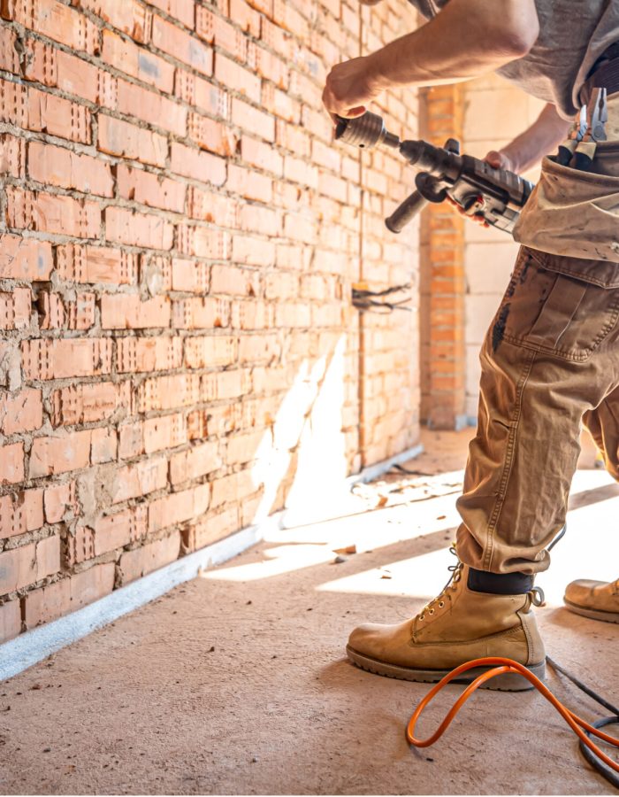 Handyman at a construction site in the process of drilling a wall with a perforator.